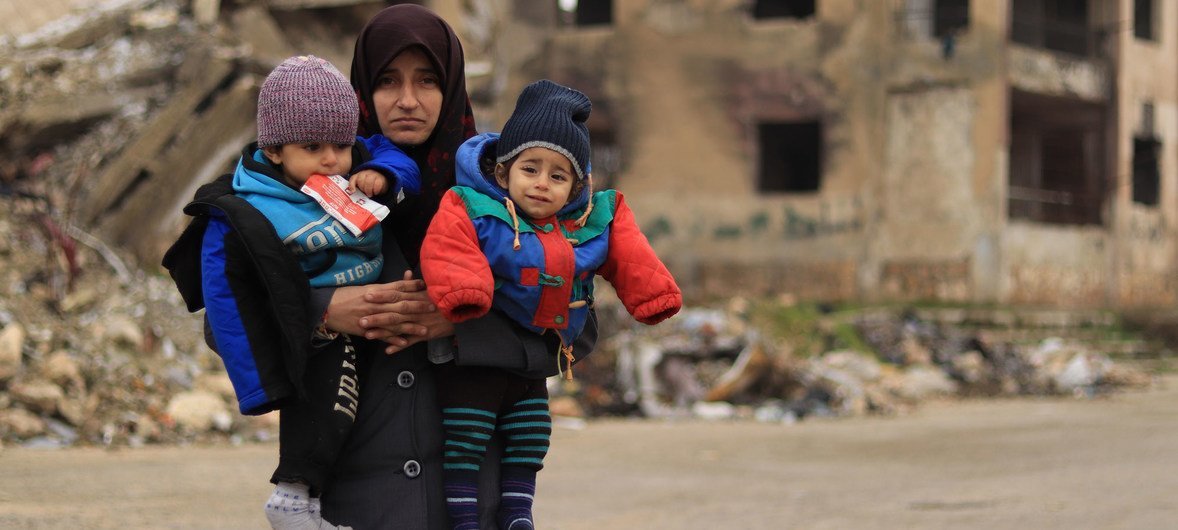 سيّدة تحمل طفليْها في مدينة حلب التي تعرّضت للدمار في سوريا